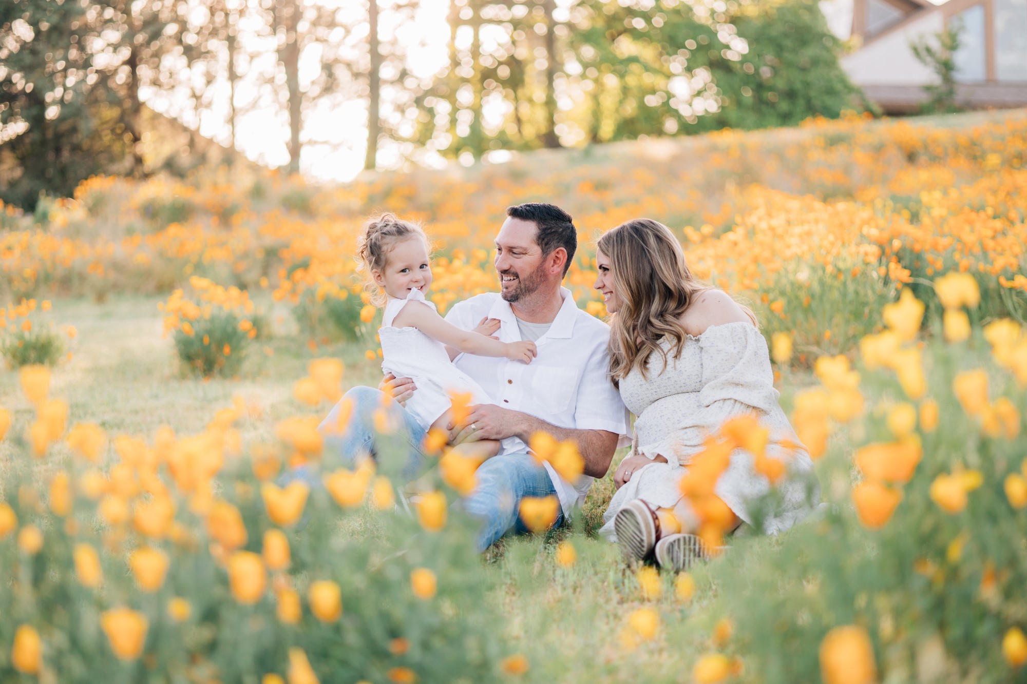 Parents wearing white holding baby and sitting in yellow flower field together