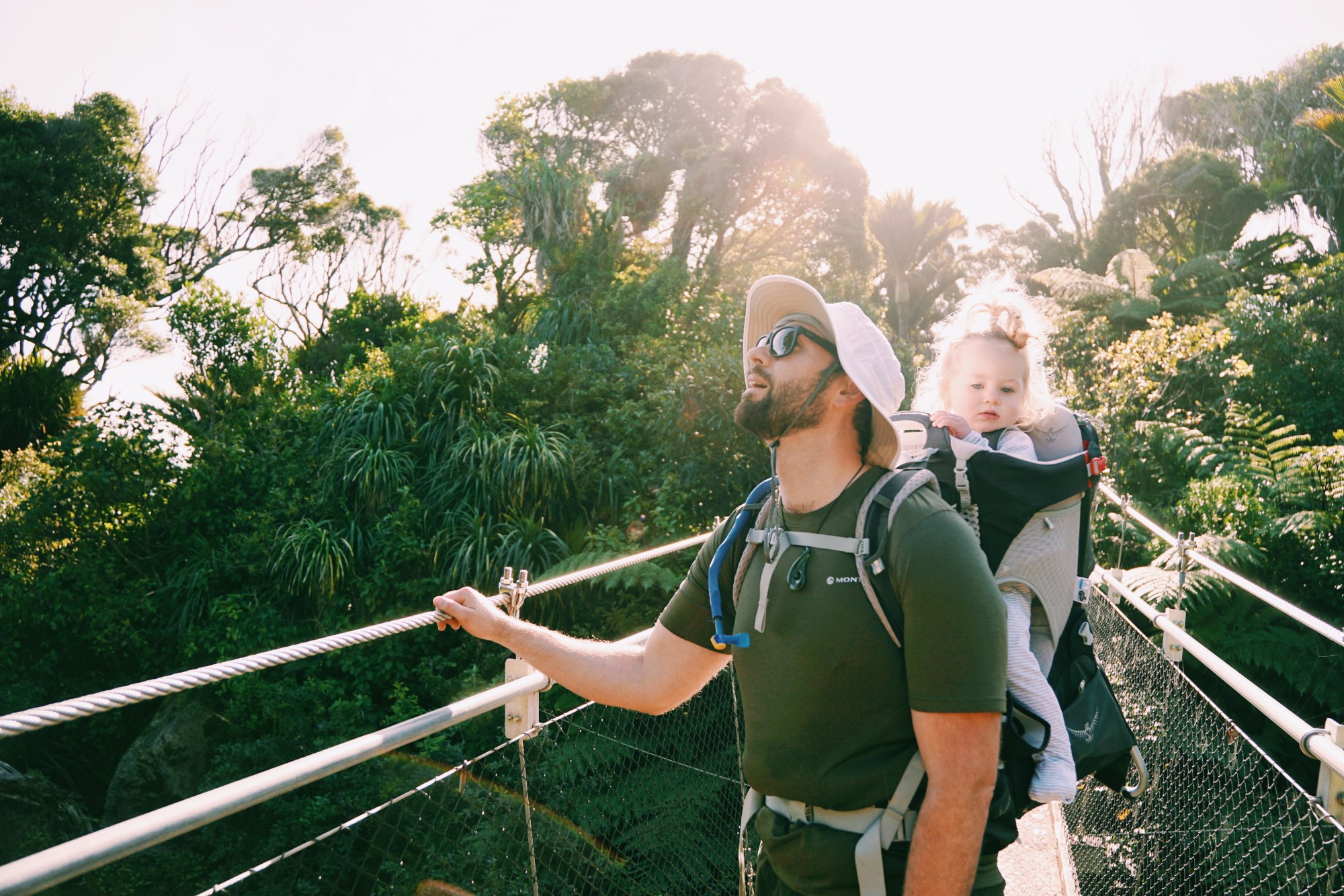 Father with baby on back backpack walk over bridge in forest looking at the sky