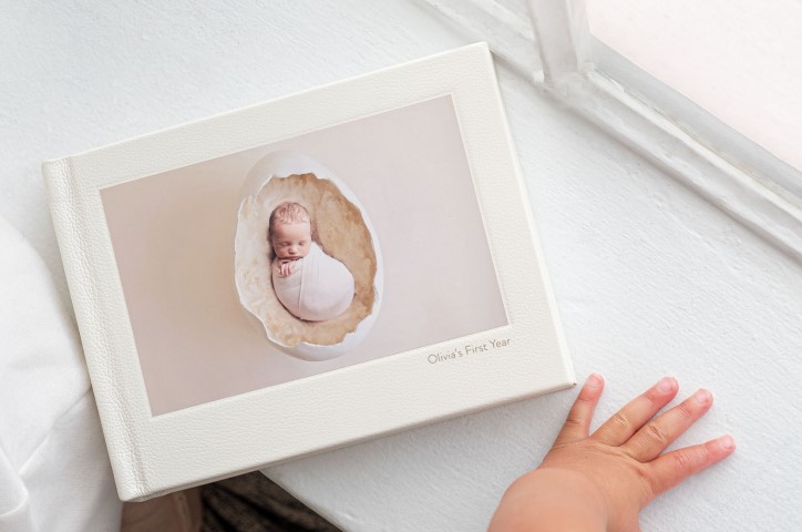 White linen landscape photo book on white table with baby on cover titled Olivia's First Year