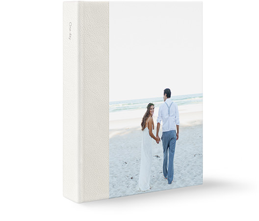A large leather portrait wedding photo album with a newlywed couple at the beach on the cover.
