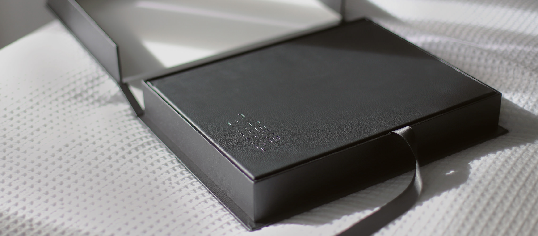 Álbum de retratos grande de couro preto dentro de uma caixa de apresentação de buckram preta em uma cama