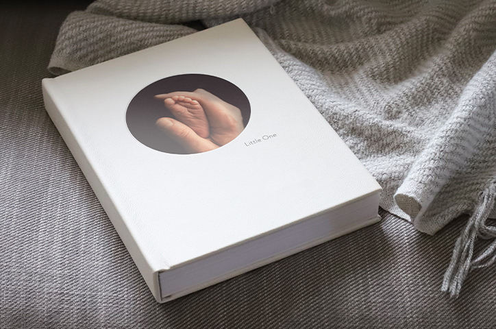 Large Portrait Baby Photo Book lying on grey couch with soft throw.