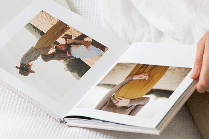 Open square photo book on white bed sheets with maternity photos on pages