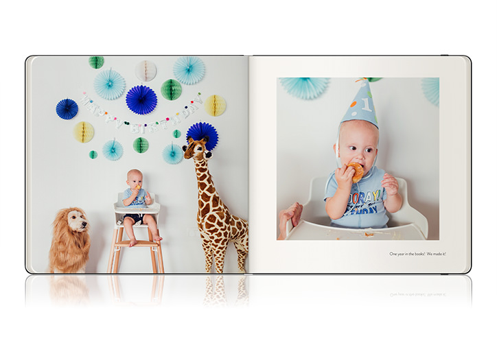 Open Moleskine photo book with baby in high chair eating a sandwich wearing party hat during blue themed birthday party