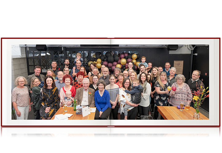 Open red photo book with widespread family group photo all smiling by wooden tables