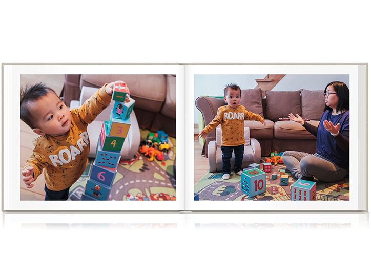 Livro de fotografias da família Paisagem aberto com duas fotos de uma mãe e seu filho brincando com brinquedos na sala de estar.