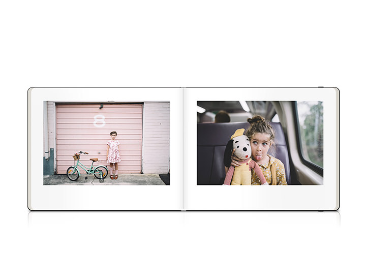 Open Moleskine photo book with little girl in car and a photo of the little girl standing in front of pink garage