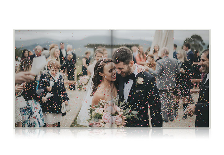Álbum de fotos de casamento paisagístico aberto com uma foto de um casal caminhando pela ilha coberta de confetis.