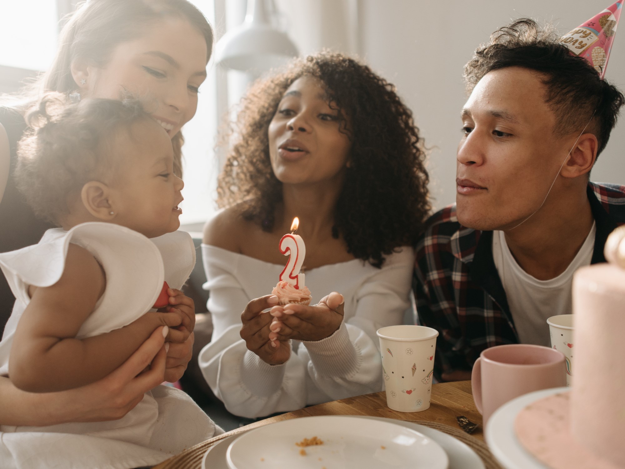 Family together holding child during birthday party encouraging them to blow number 2 shaped candle out