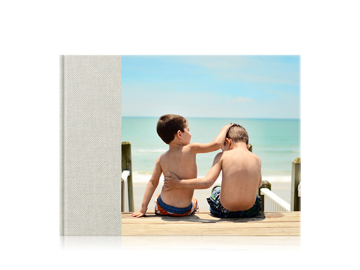 Livro fotográfico familiar premium de paisagem com uma capa de 3/4 de dois irmãos na praia com braços em volta um do outro.