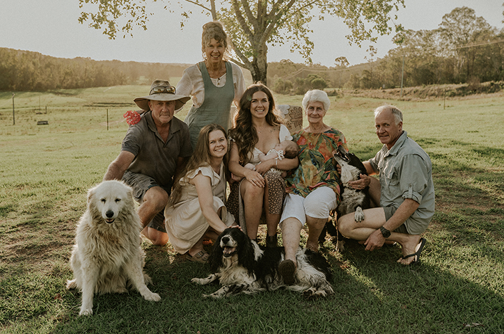 Family photo spanning generations, dogs included, in a grassy landscape.