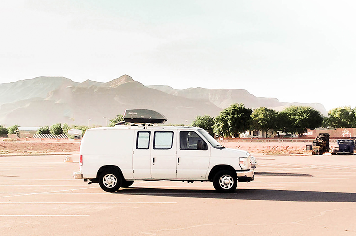White van on desert road in front of mountain.