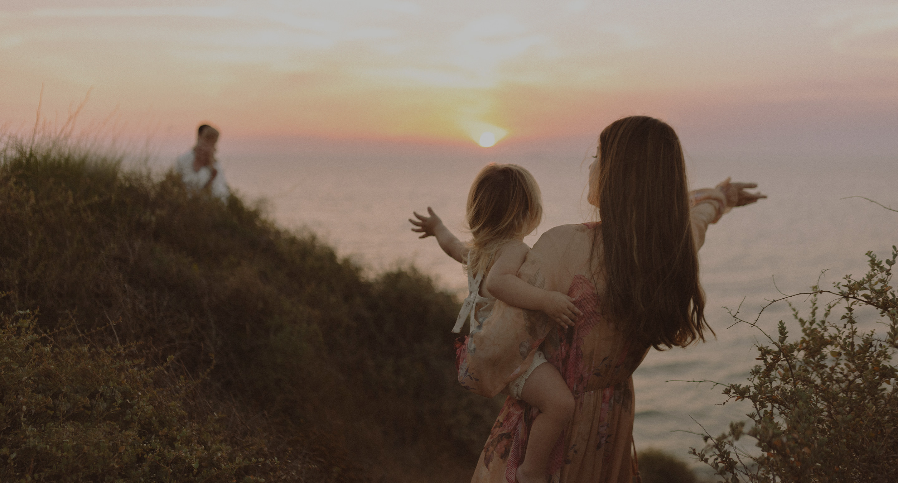 Mamãe com a filha nos braços assistindo ao pôr do sol.