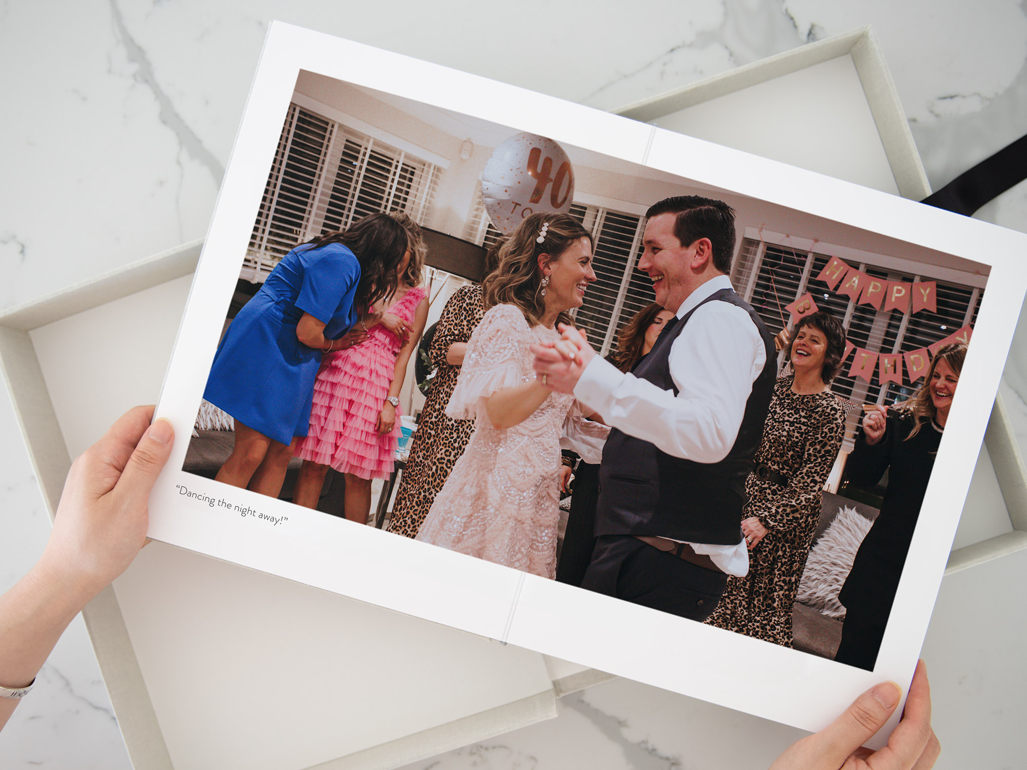 Open photo book being held pages show couple dancing at birthday party wearing pink colors