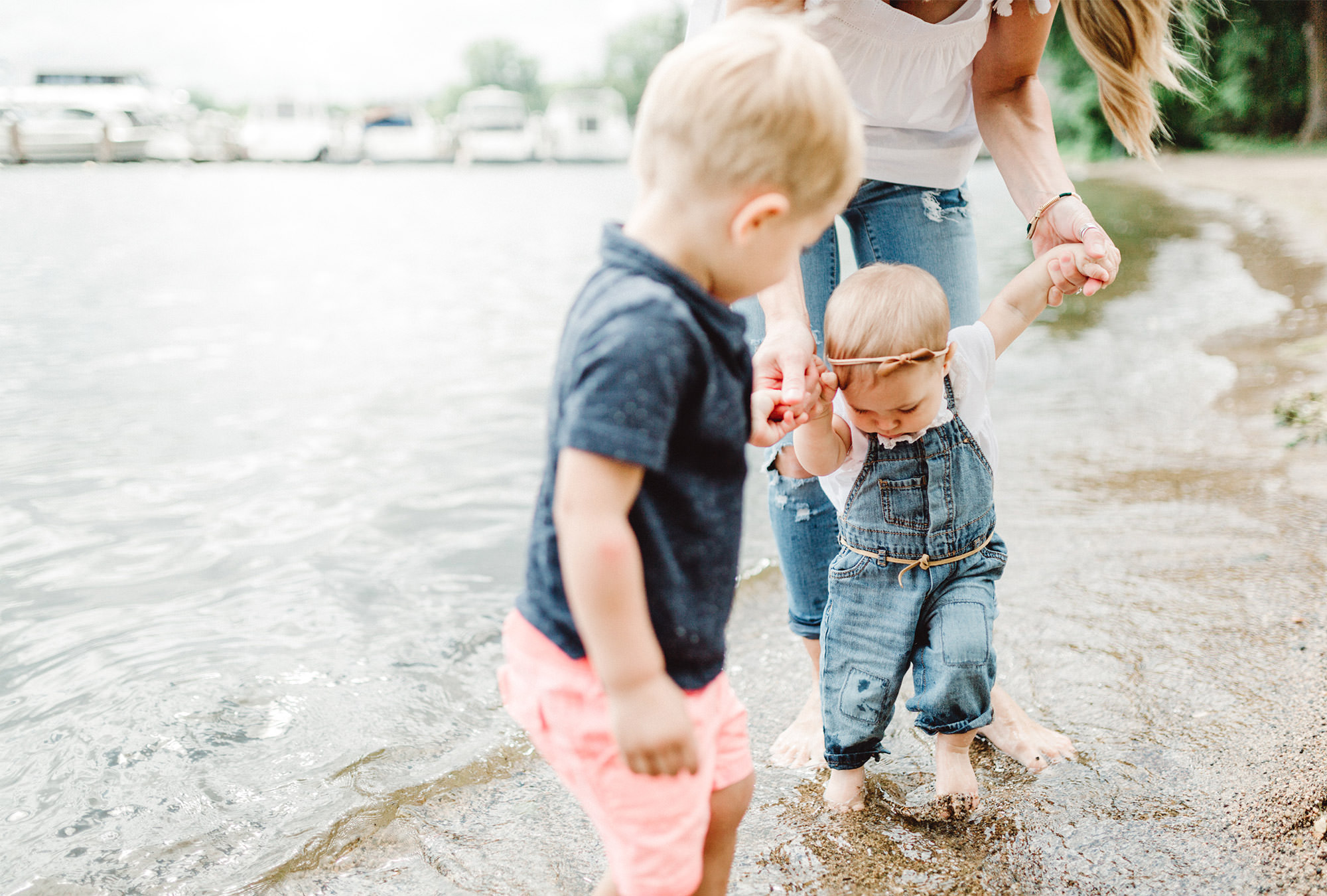 Mother holding two son's hands while wading through shallow water.