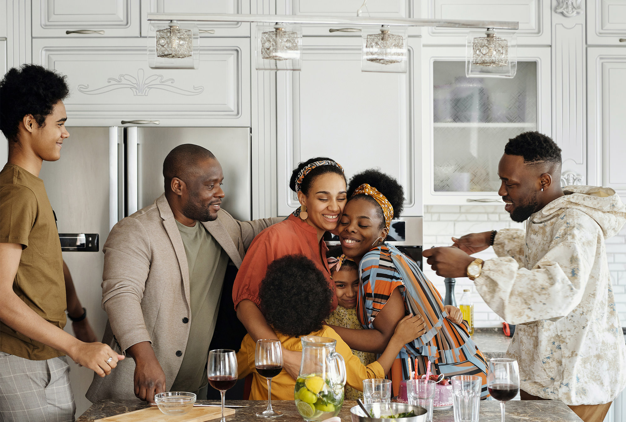 Family hugging and smiling at dining table in modern kitchen area.