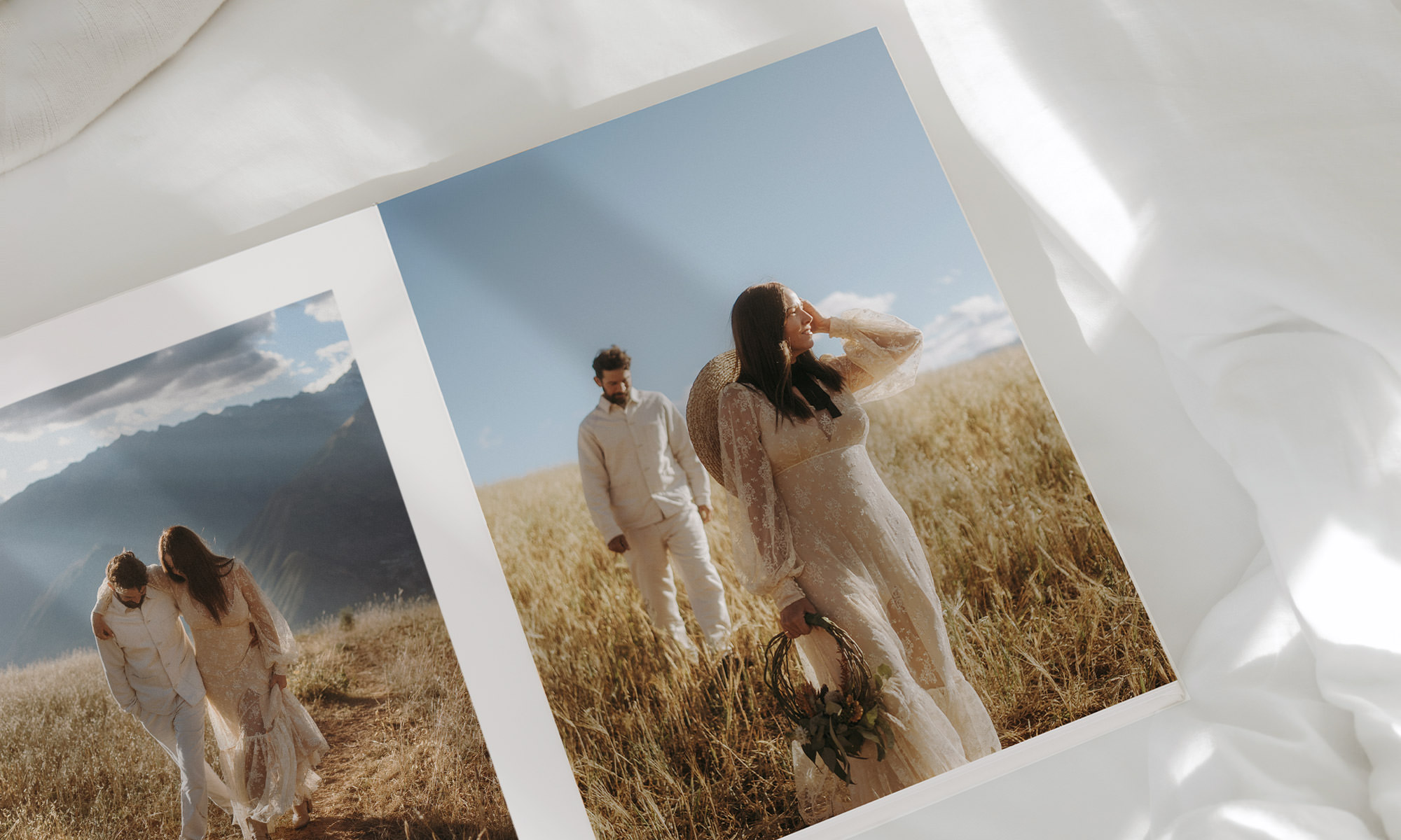 A couple in bohemian white outfits walk a dry grass hill overlooking mountains on cloudy day