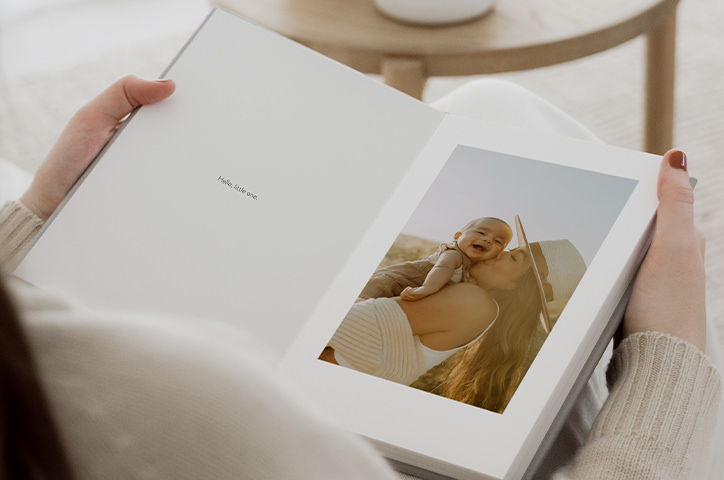Woman holding open Portrait Premium Photo Album with mother and baby photo inside