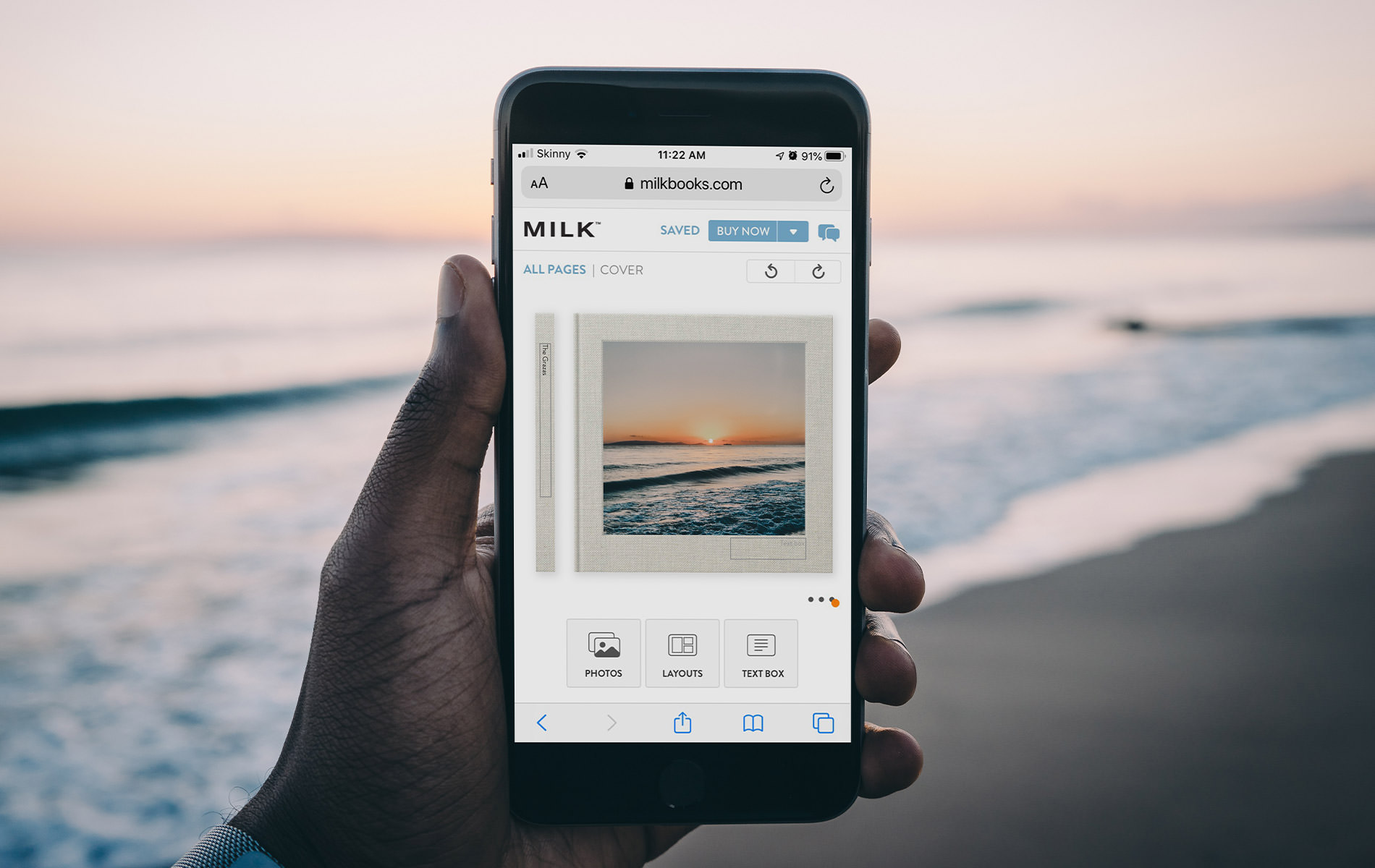Person at the beach creating a photo book with sunset image on cover.
