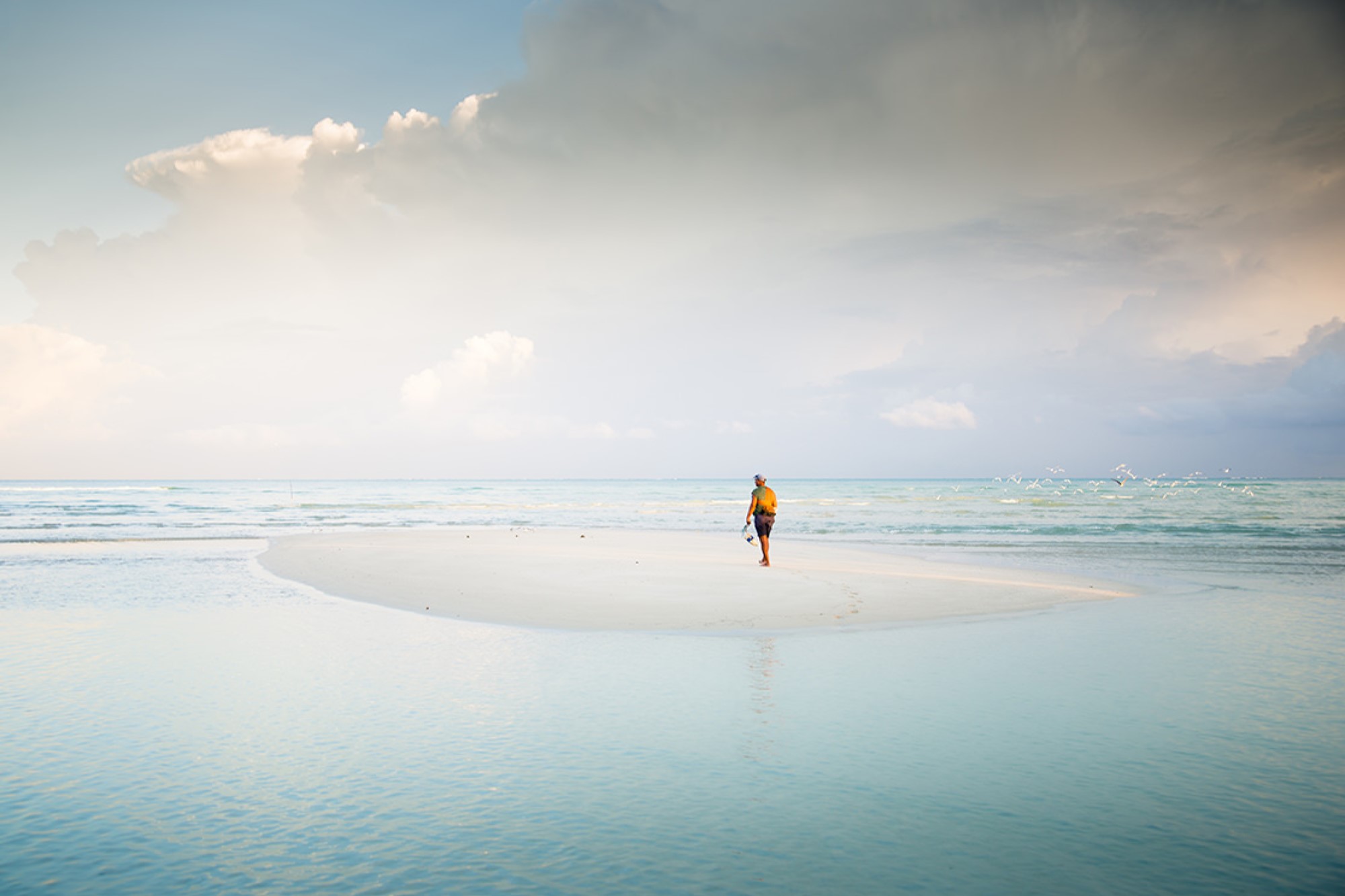 Man with camera on white sand plateau surrounded by reflective blue water and cloudy sky