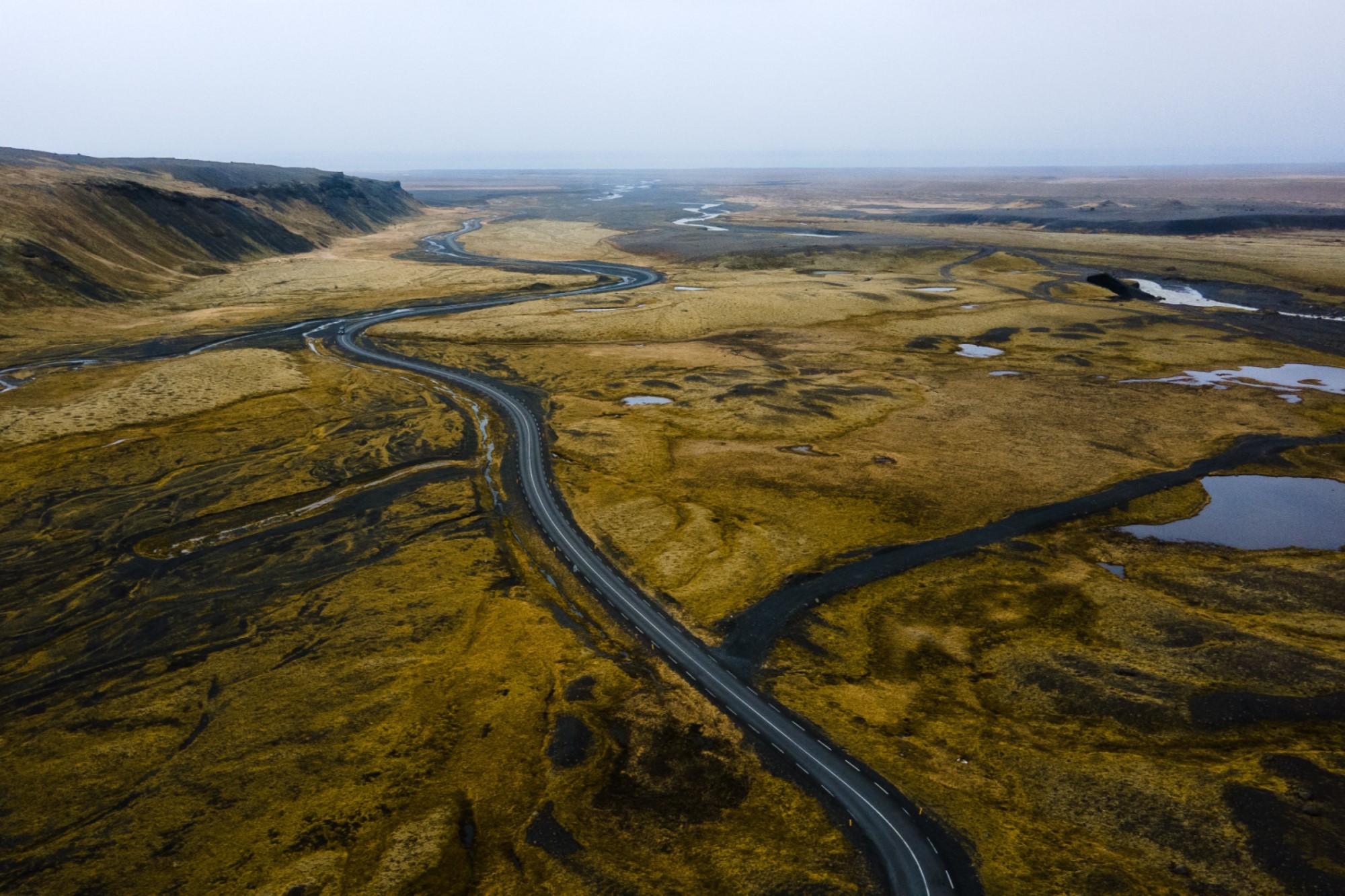 Aerial photography shot of rural flat wetland with windy road through it during cloudy misty weather