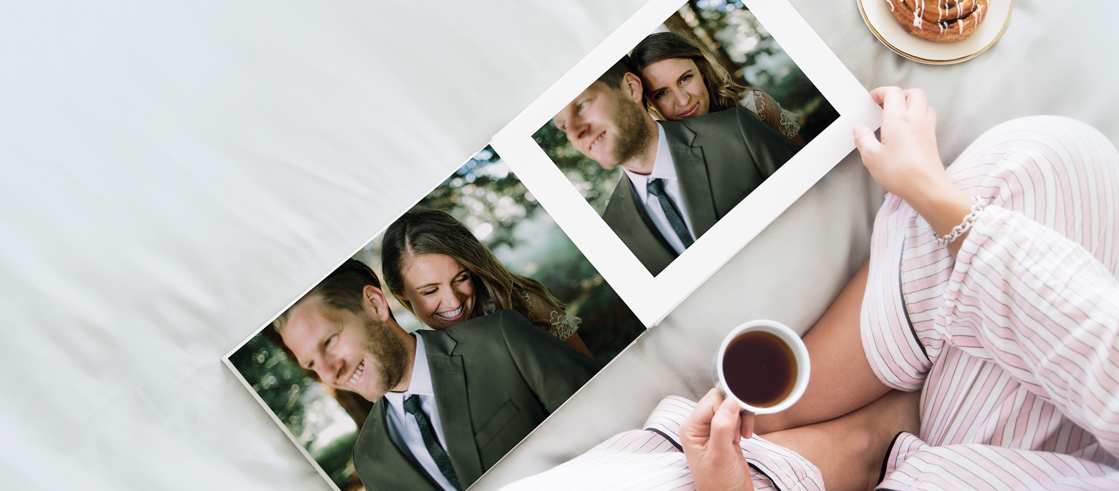 Mulher olhando através de seu álbum de fotos de casamento de paisagem plana na cama com um café na mão.