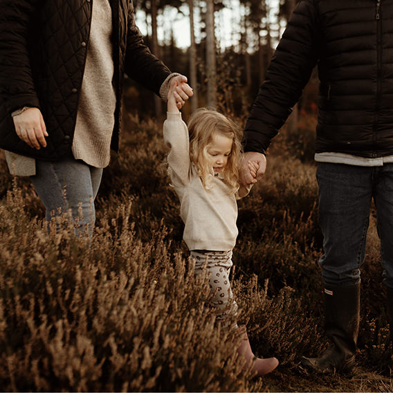 Little girl holding parent's hands as they walk through a field at dusk.