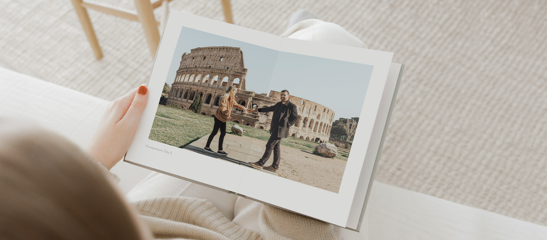 Mulher senta-se em uma cama branca e olha o álbum de fotos de Roma aberto.
