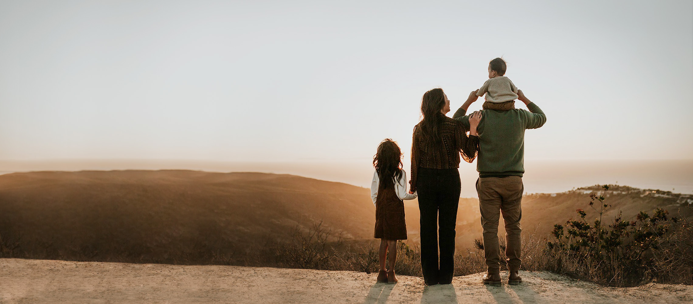 Family of four watch sunset together on edge of cliff