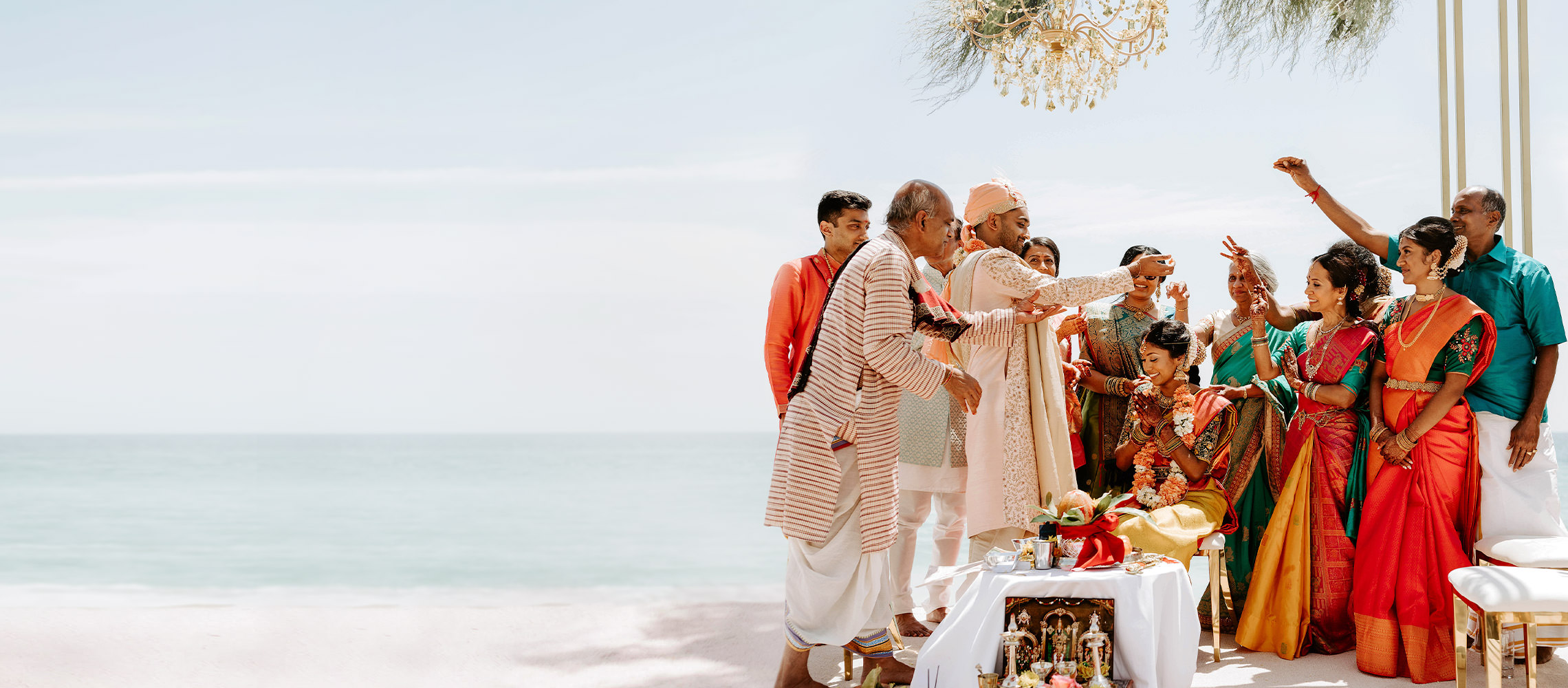 Indian wedding on beach with bright green and orange outfits.