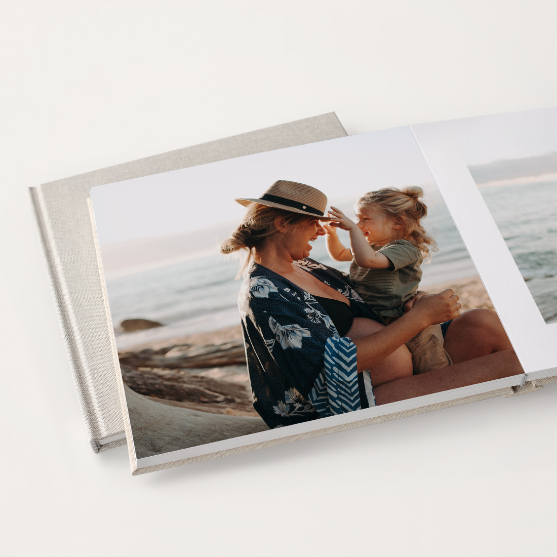 Two beige linin square photo books with mother and child together happily on the beach on its pages