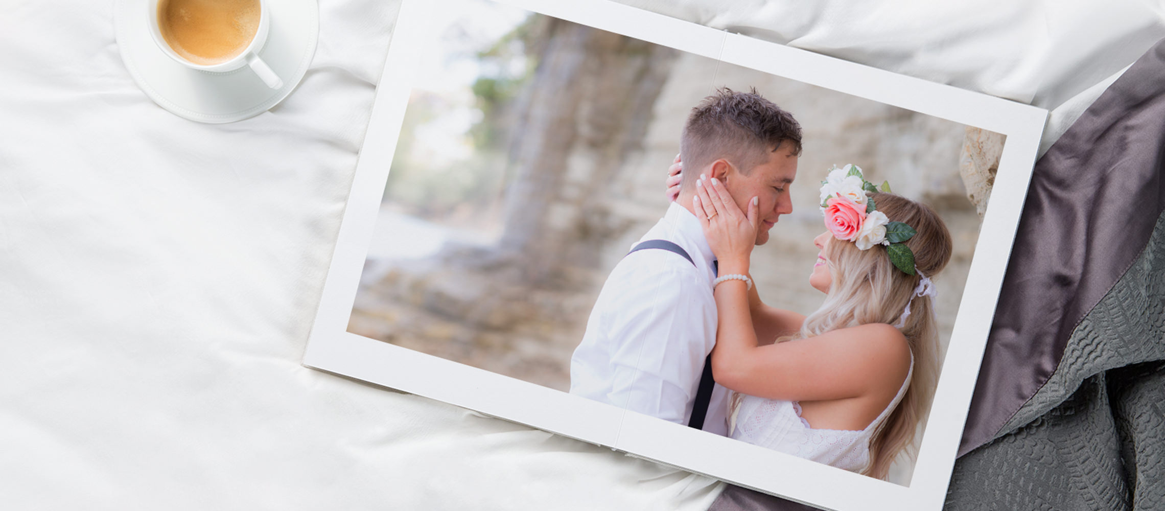 Álbum de noivado em uma cama com casal apaixonado na capa. Ao lado do álbum há uma xícara de café.