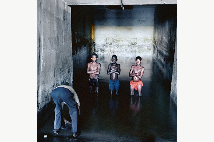 Three boys with a man bending over to take a photo in a cement walled room in South Africa