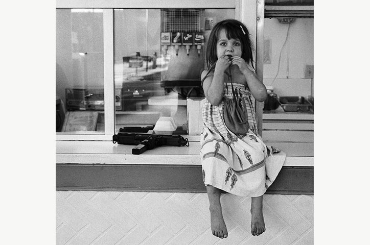 Monochrome photo of young girl sitting on diner counter while eating messily