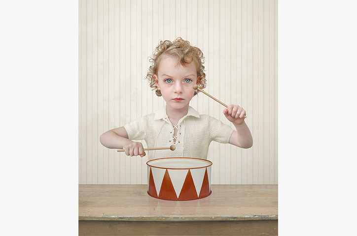 Curly haired child drumming with straight expression on wooden table
