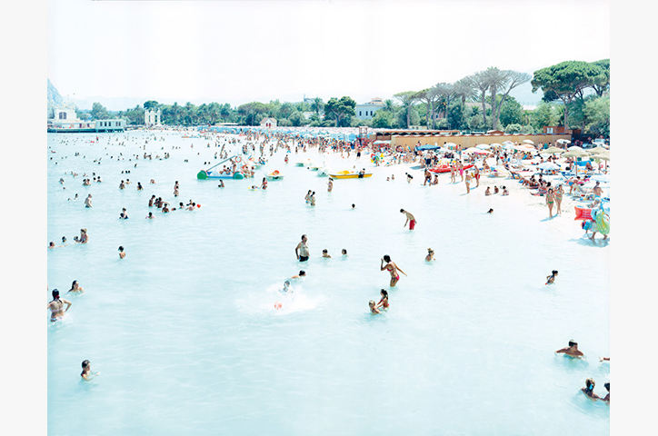 Wide shot of pale blue beach with thousands of swimmers and beach loungers