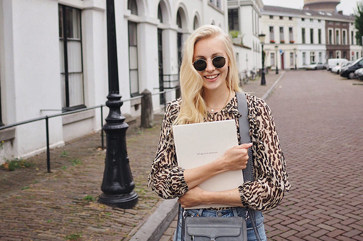 Blonde woman with black round glasses holding MILK photo book in cobbled street