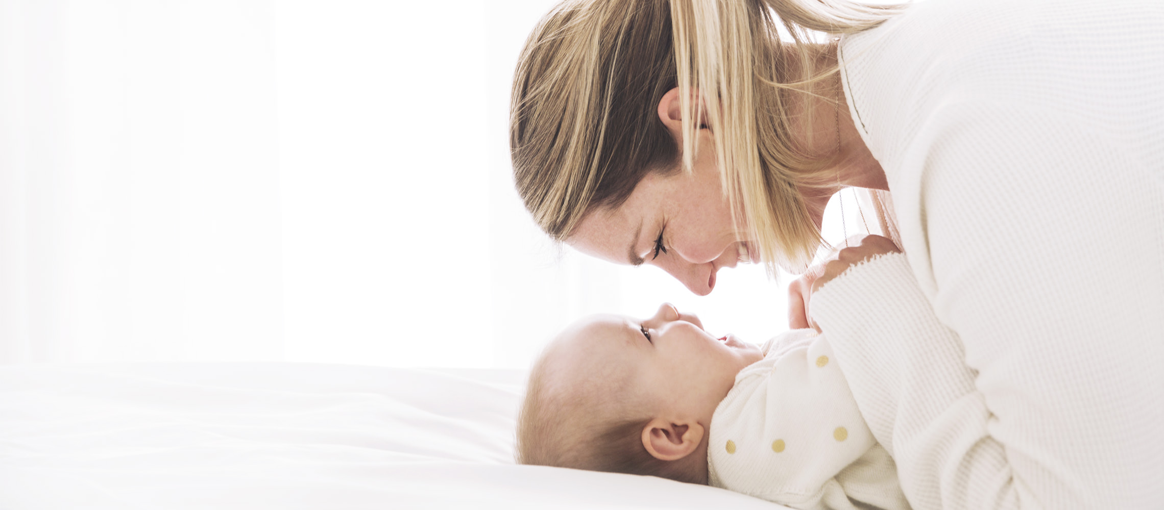 Mãe e bebê olham nos olhos um do outro de muito perto, sorrindo.