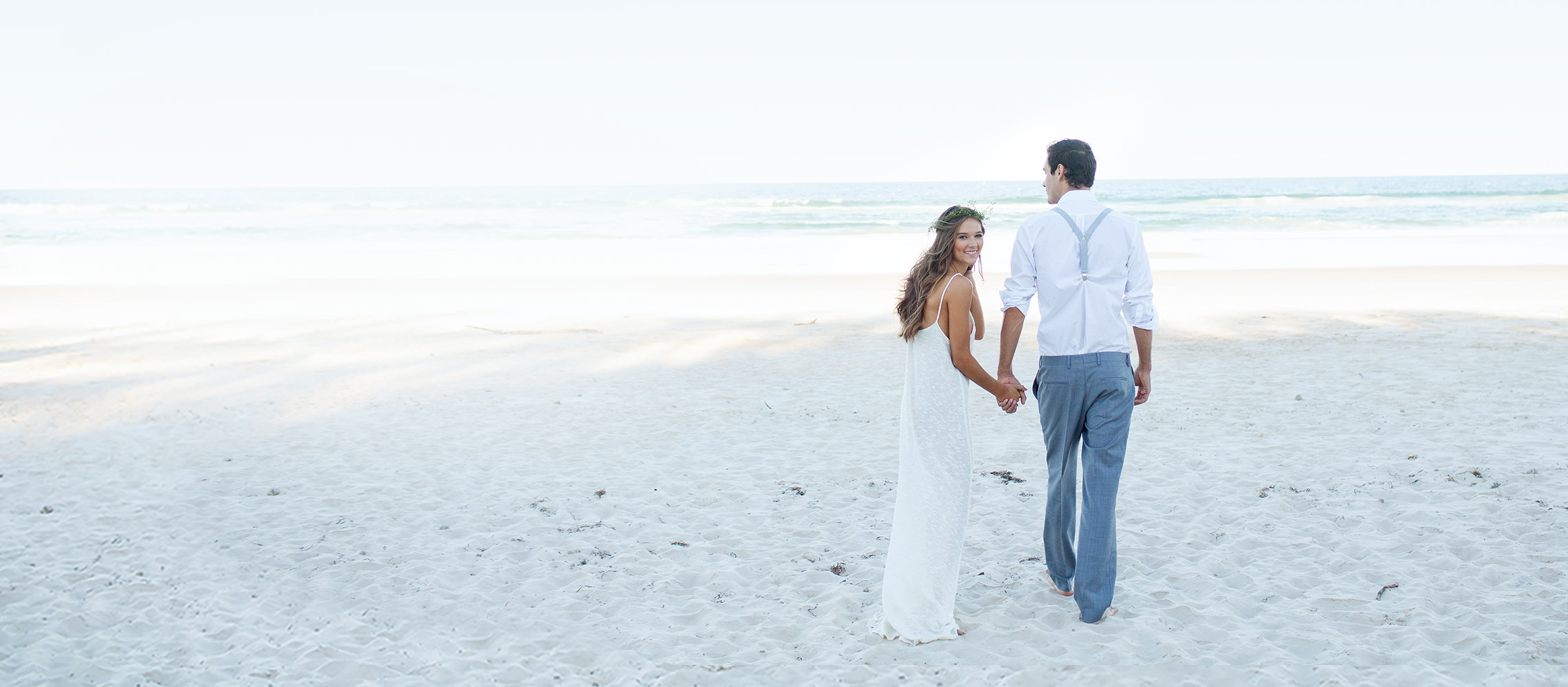 Os noivos andam descalços em direção ao mar.