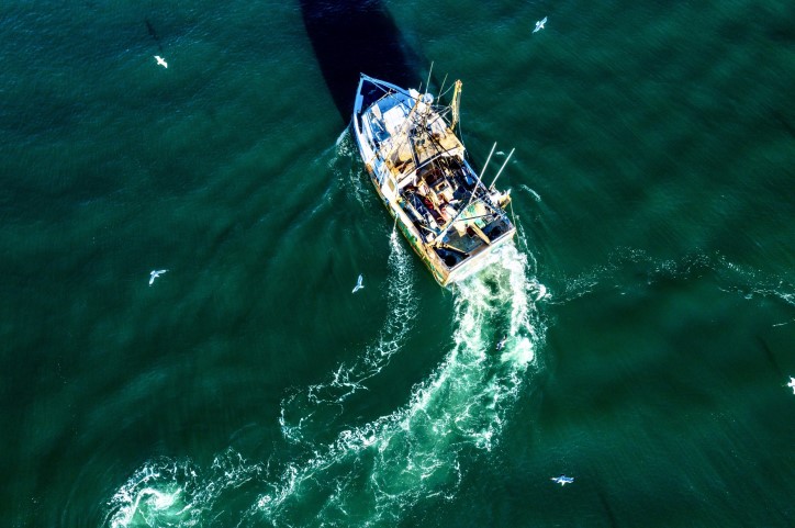 Aerial photo of fishing boat leaving wave trail on on dark aqua sea