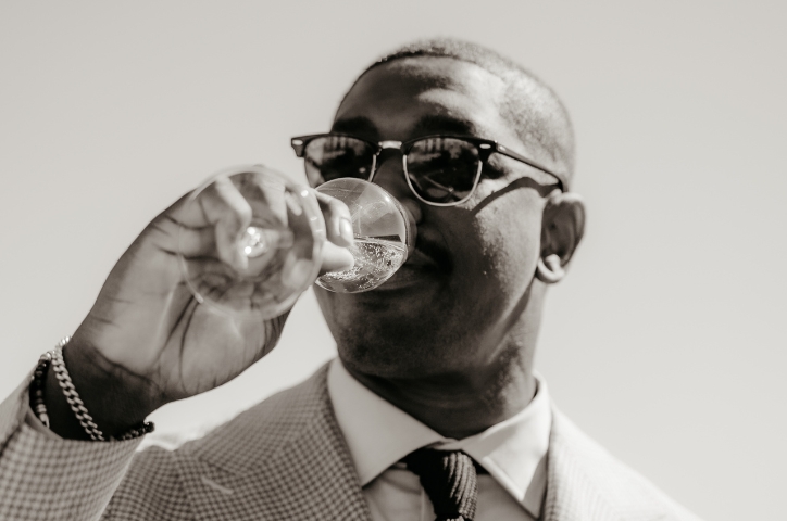 Black and white photo of a groom wearing sunglasses drinking champagne.