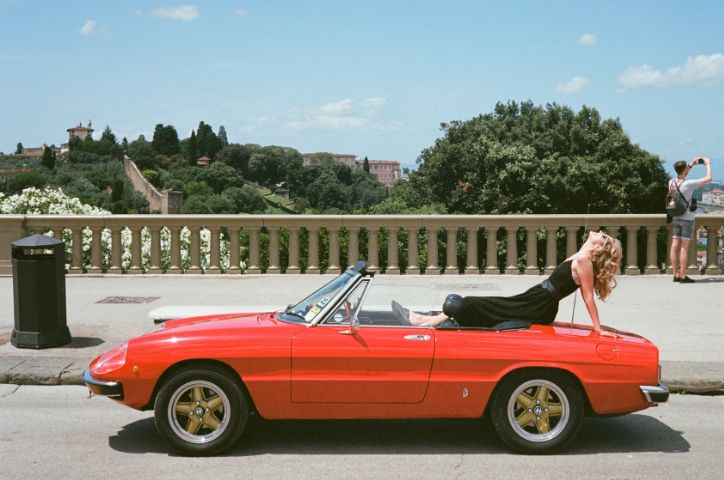 Woman lies back on the end of a red convertible on a sunny day in Florence Italy
