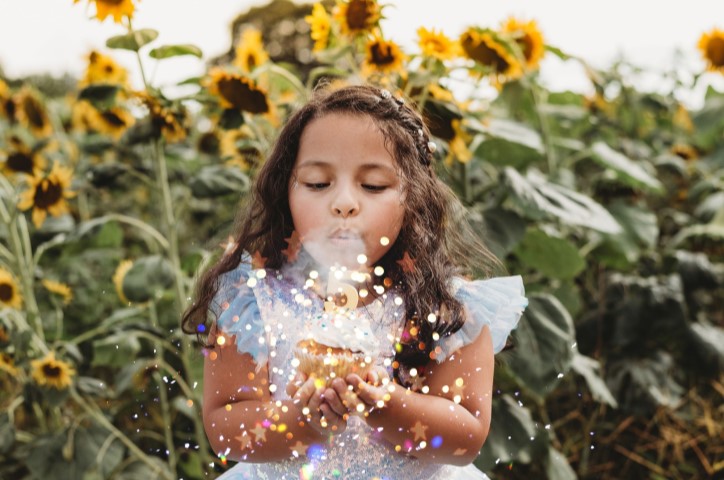 Young girl in front of sunflowers blowing out 5th birthday candle on cupcake