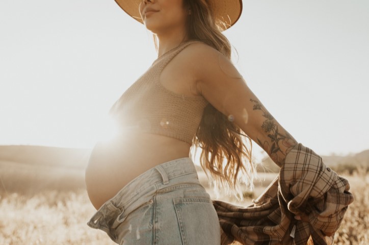 Pregnant woman stretches in front of sunrise in dried grass field