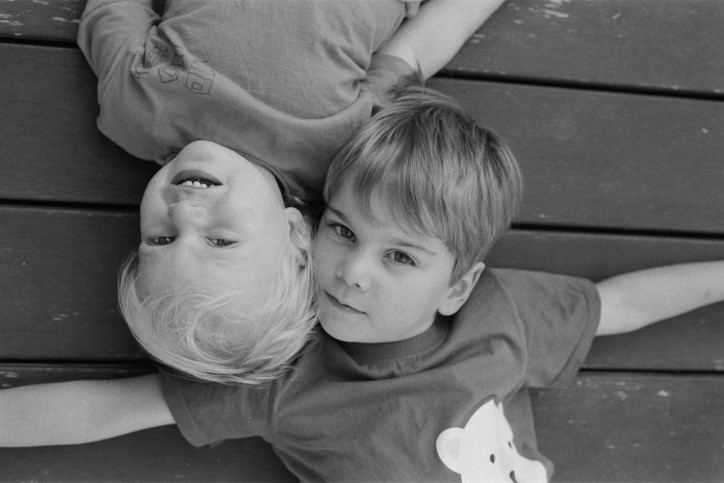 Black and white photo of two young boy brothers lying on wooden deck