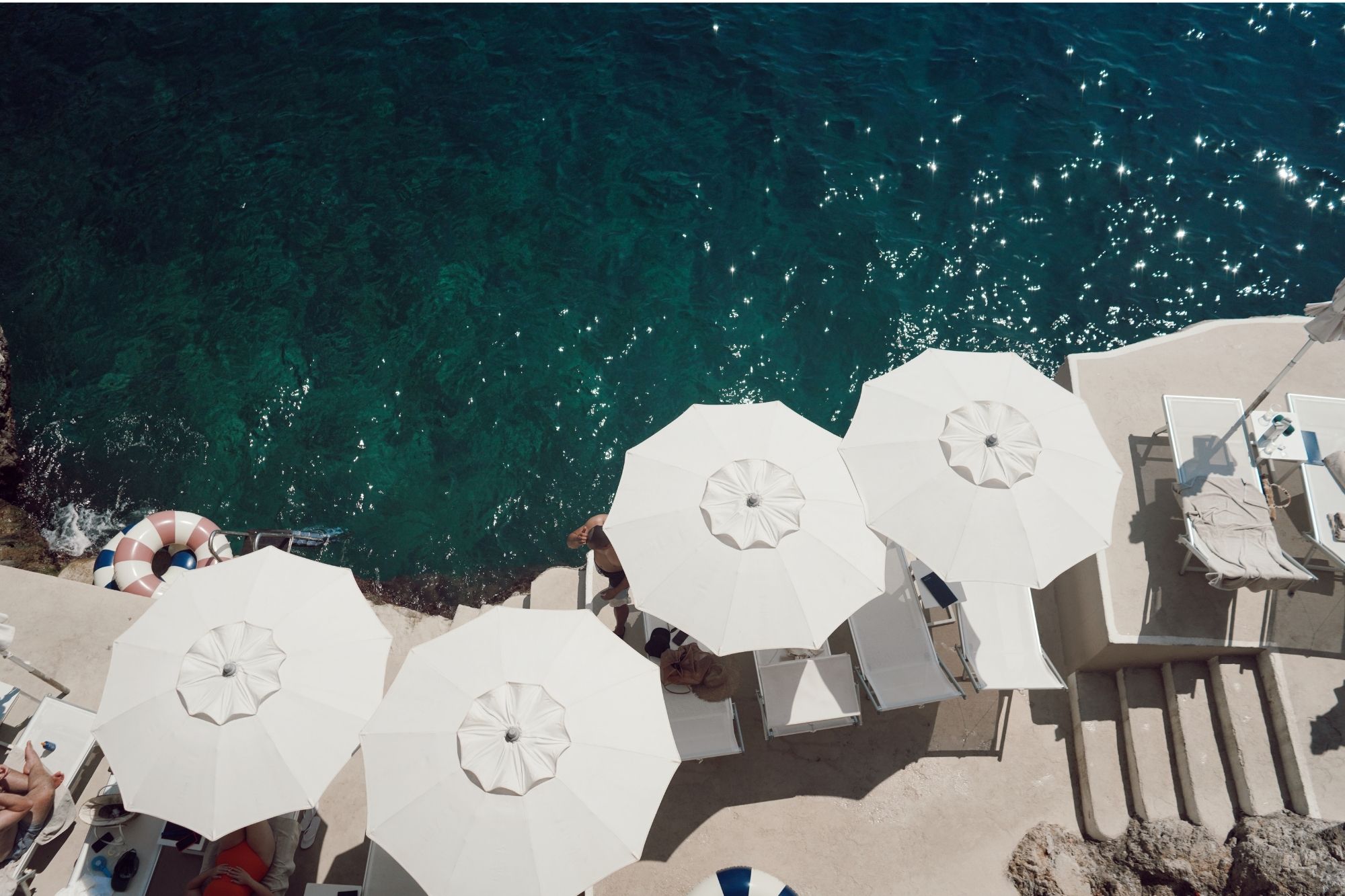 Aerial shot of ocean next to the beach chair and umbrella setting