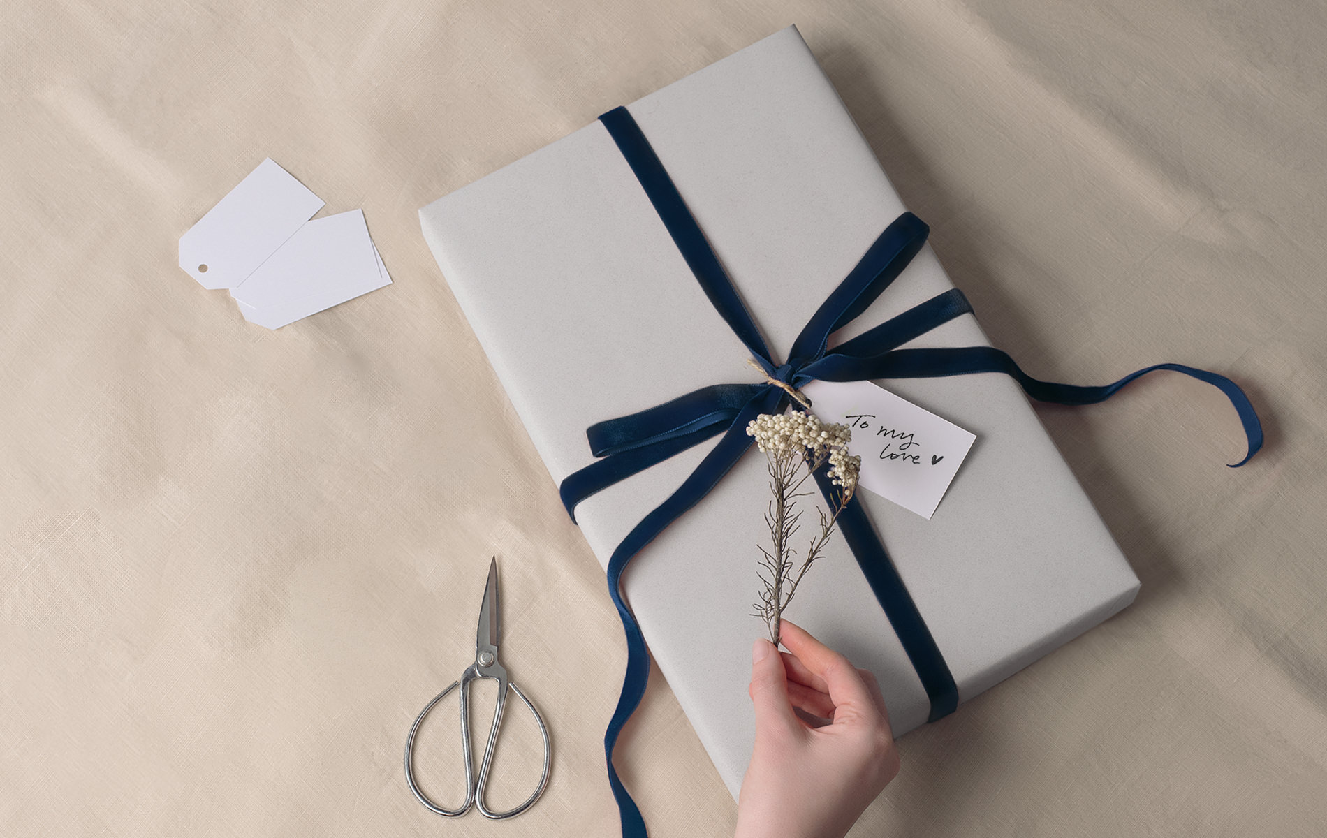 Hand tying a linen giftbox on parchment with silver scissors next to box
