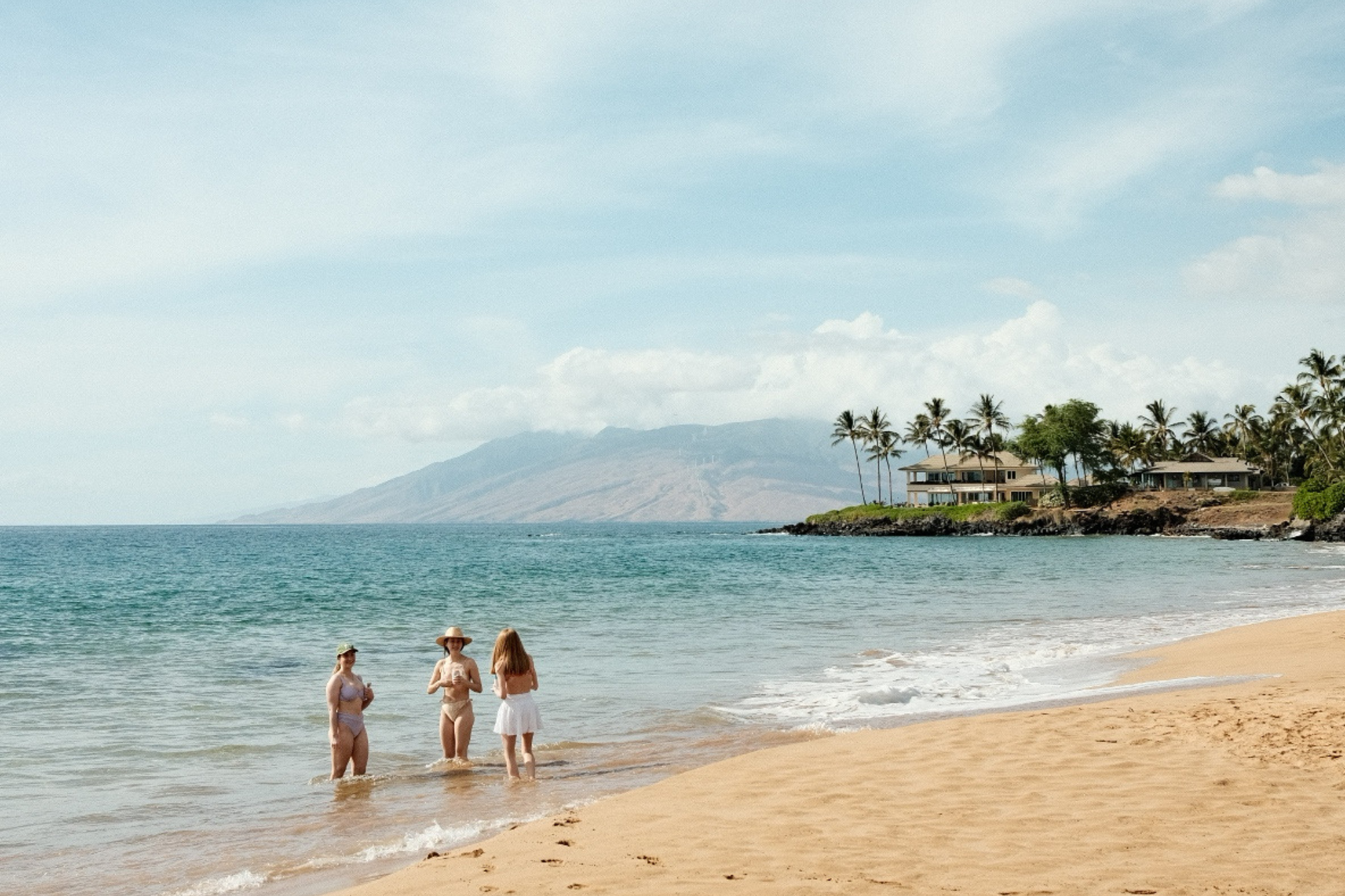 Three women in bikinis stand in shallow water on sunny beach in Maui Hawaii