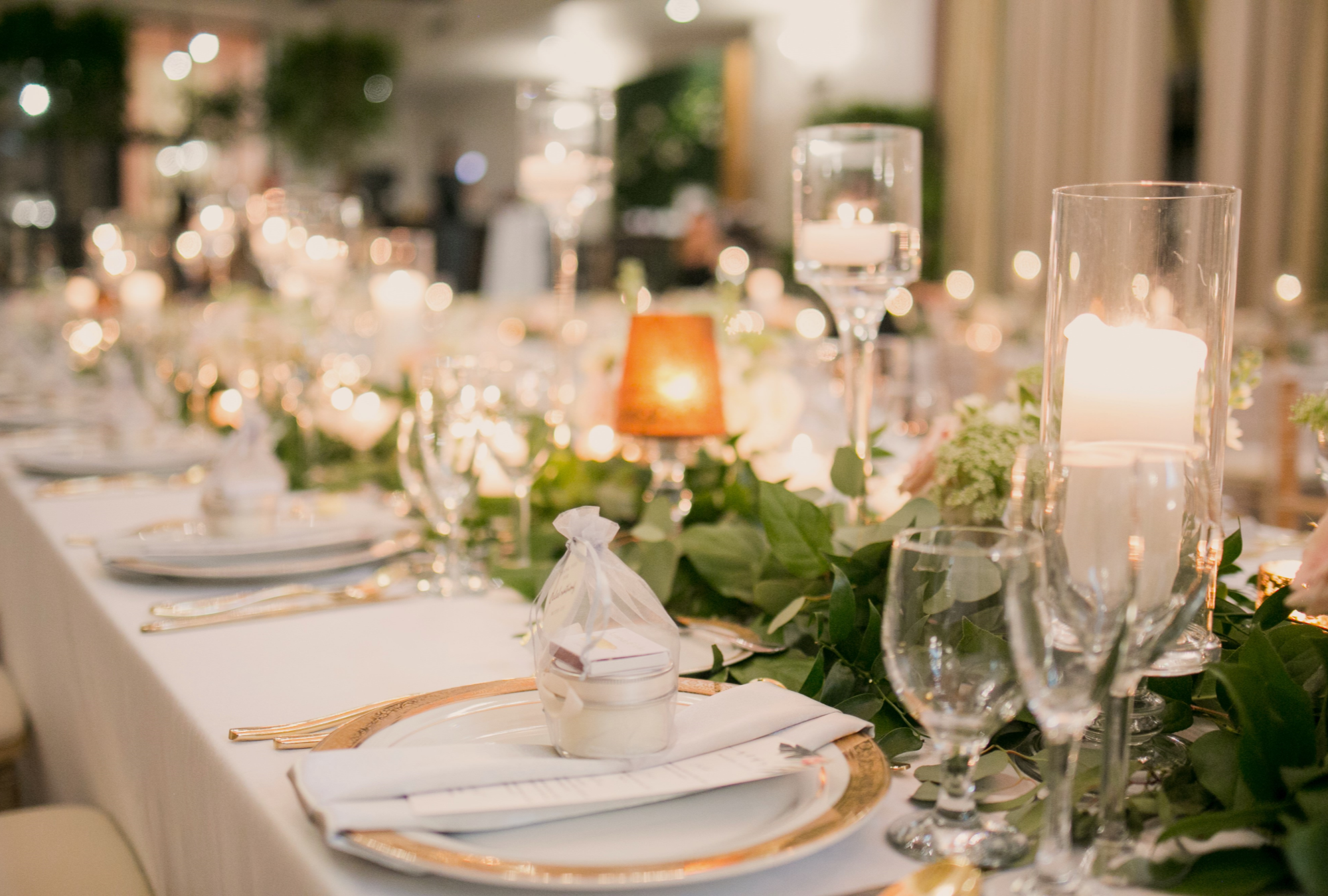 Wedding table setting with white cloth and warm candle lighting with mini bags with a small white candle in each wedding favor