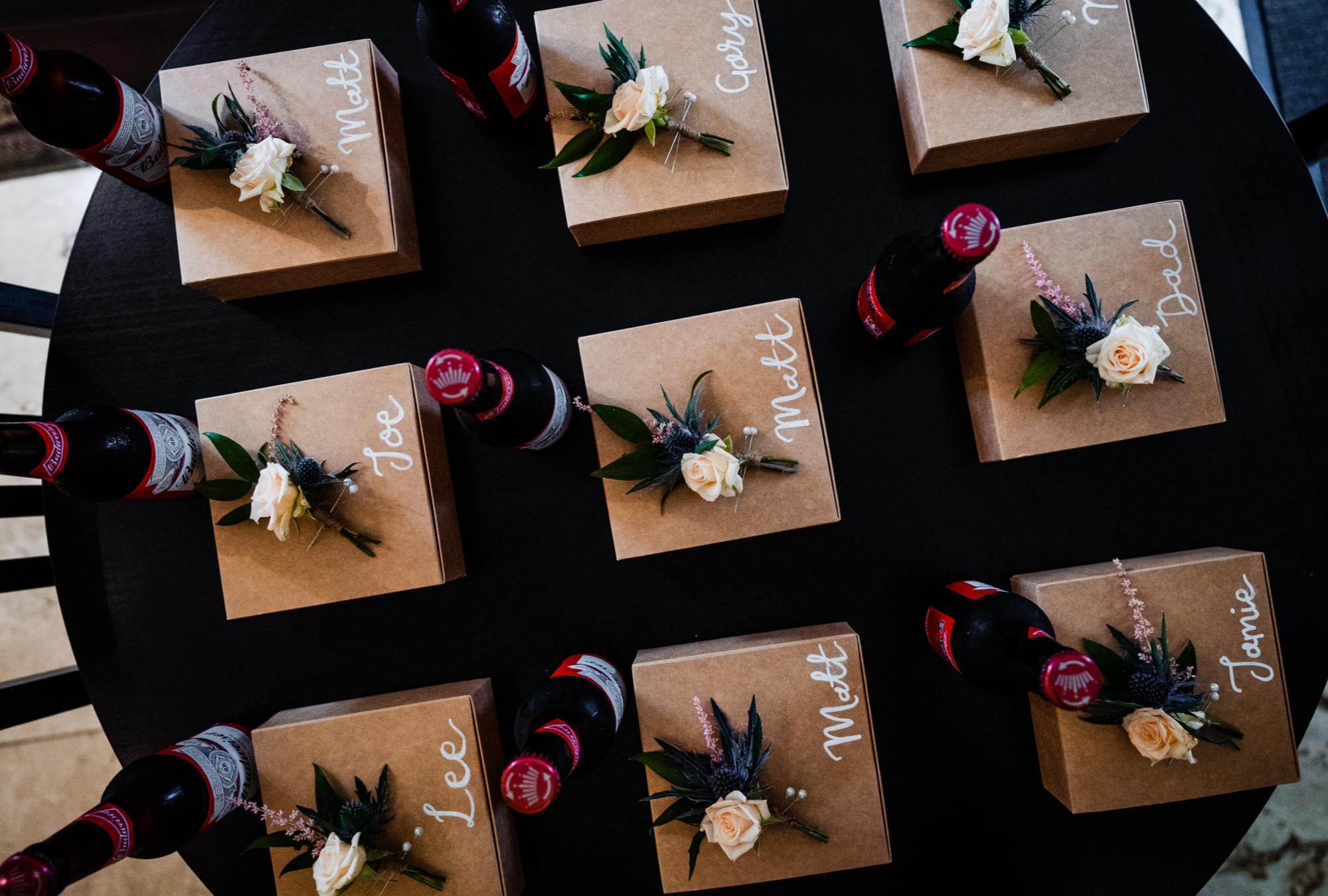 Black table with small cardboard gift boxes laid in grid layout with white flower on top and beer on the side